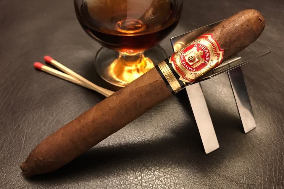 Arturo Fuente Hemingway Short Story cigar on metal stand with whiskey glass and wooden matches