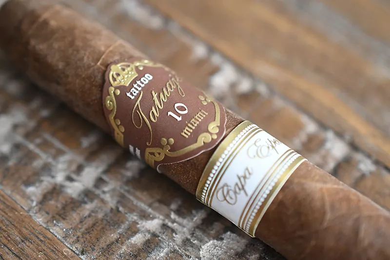 Tatuaje 10th Anniversary Capa Especial cigar with brown and gold band displaying its oily Ecuadorian Habano wrapper on a rustic wooden surface
